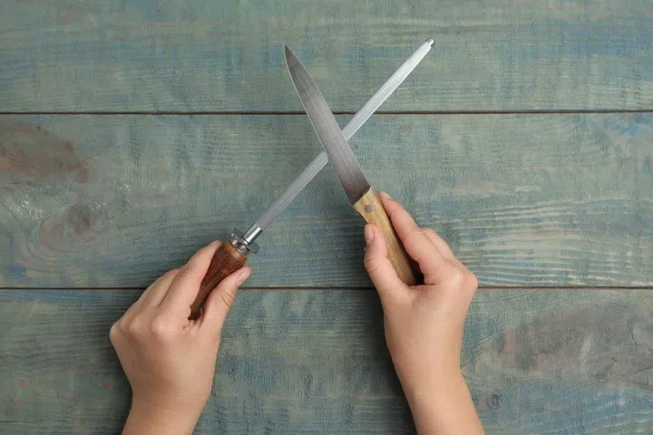Woman sharpening knife at light blue wooden table, top view.
