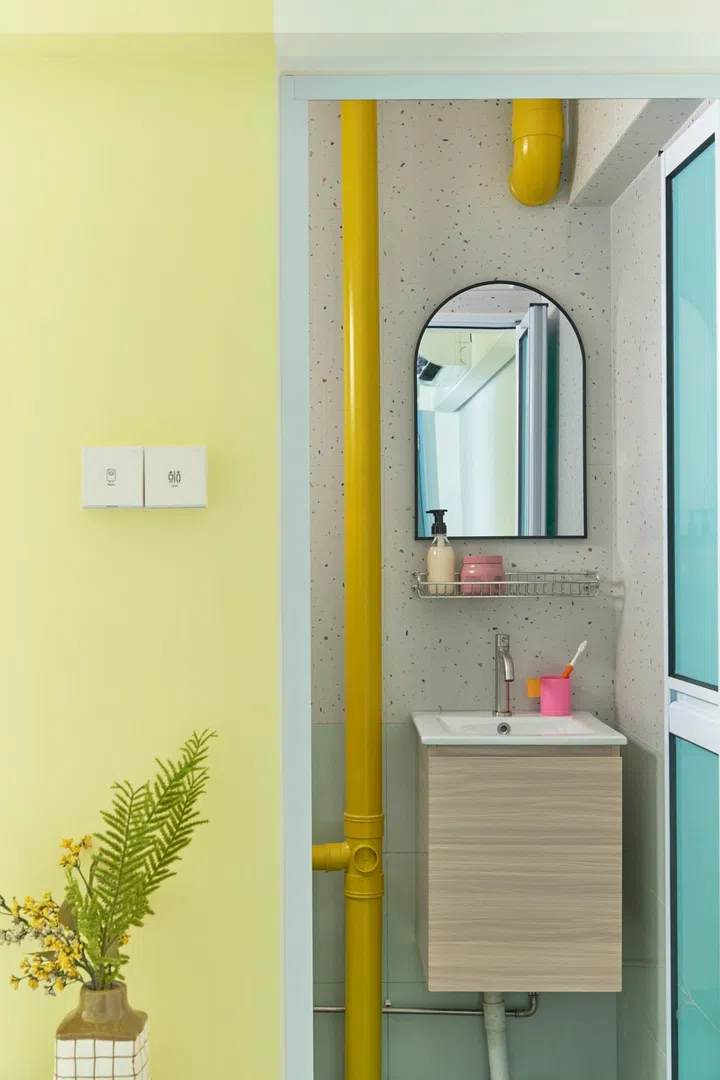 A powder blue doorframe contrasts with the Nippon Baby Breath 1163 yellow wall. The permanent bathroom pipe was painted in Nippon Sunlight 1190. The bottom tiles are another blue/green tone (Lian Seng Hin - GC-36P3076), balanced by terrazzo-inspired upper walls, Lian Seng Hin - 01-AGT602121R. 