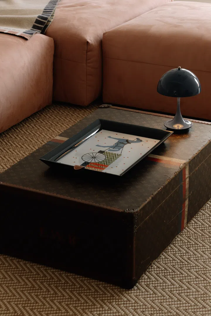 A vintage Louis Vuitton trunk finds new life as a coffee table, paired with a Louis Poulsen Panthella portable lamp that reflects the couple’s appreciation for timeless European design.