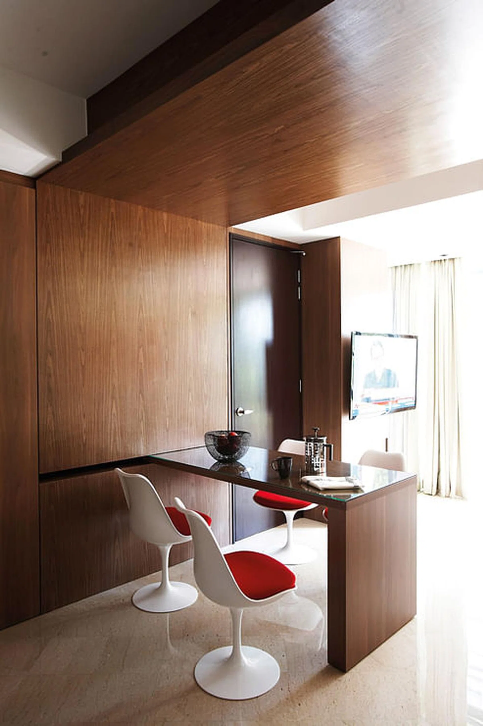 A painting from Ode to Art adds a pop of colour to the woody hues of the apartment, as do the Tulip chairs from Dream Interiors. Sofa from B&W. Cabinet and barstool from Xtra Park Mall. Interior design by Homme Space