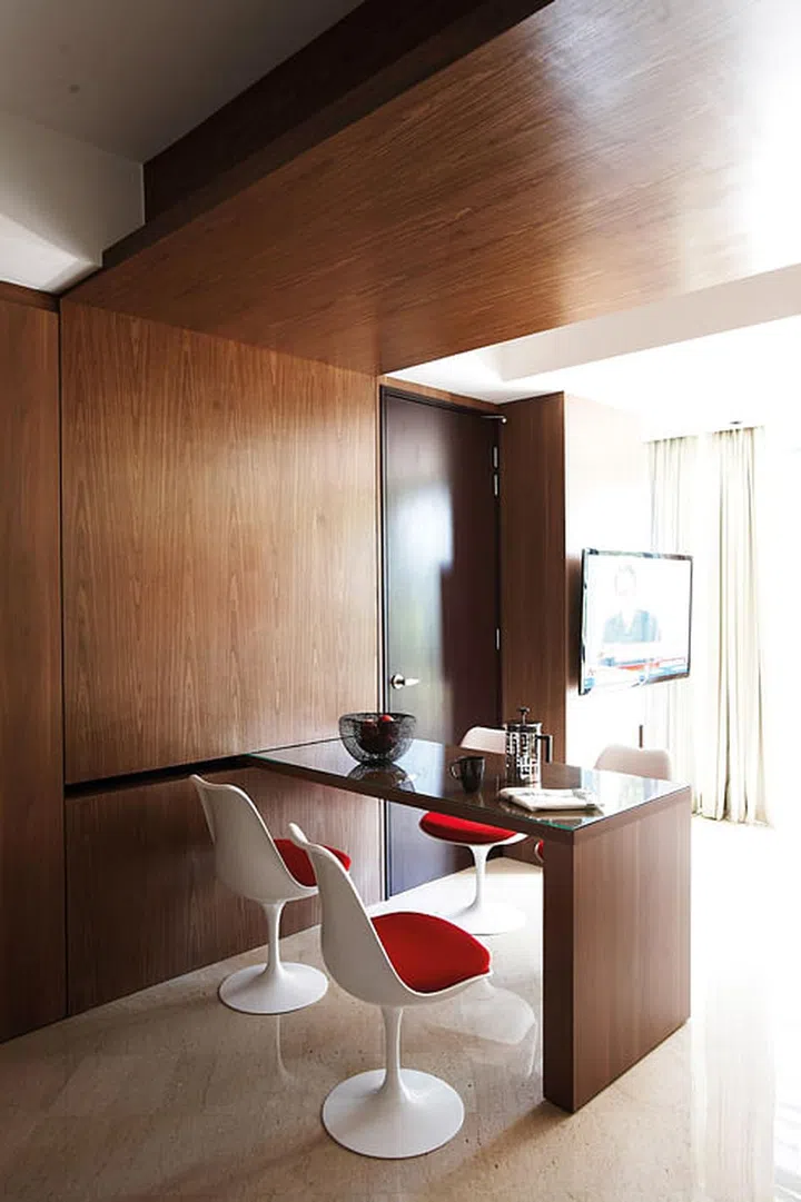 A painting from Ode to Art adds a pop of colour to the woody hues of the apartment, as do the Tulip chairs from Dream Interiors. Sofa from B&W. Cabinet and barstool from Xtra Park Mall. Interior design by Homme Space