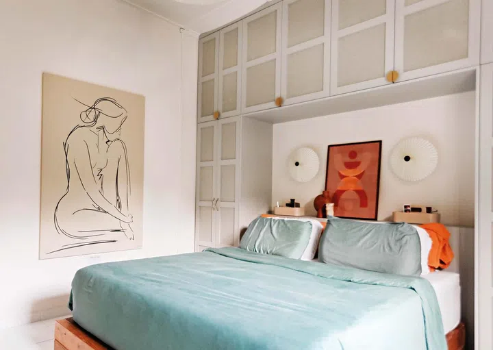 A double bed with blue bedsheets, with a panting on the wall
