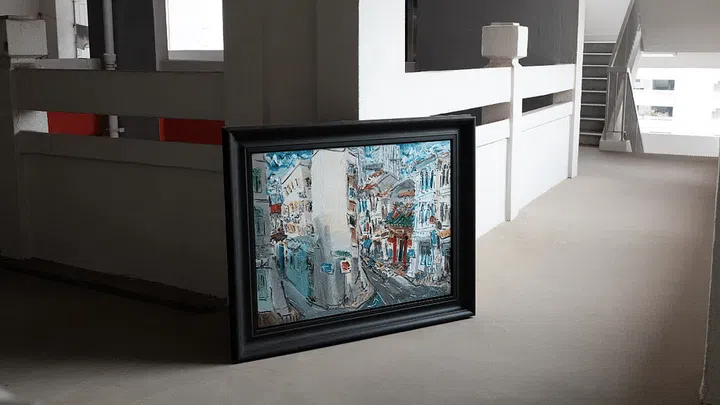 A piece of framed art sitting at the corner of a corridor.