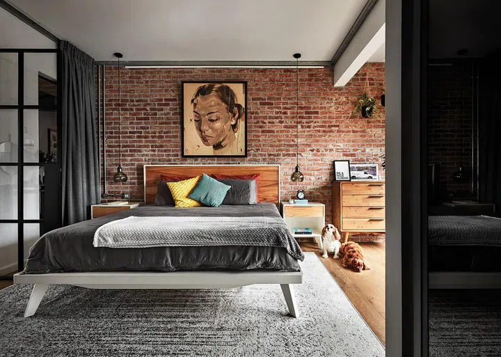 The master bedroom is enclosed via black- framed glass doors juxtaposing against the earthy brick wall.