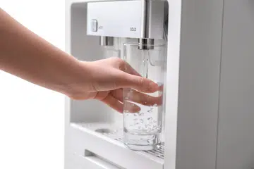 Woman filling glass with water from cooler, closeup.