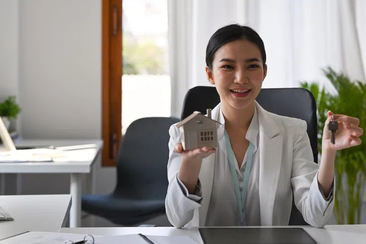 Female real estate agent holding house model and keys. Mortgage and real estate investment concept.