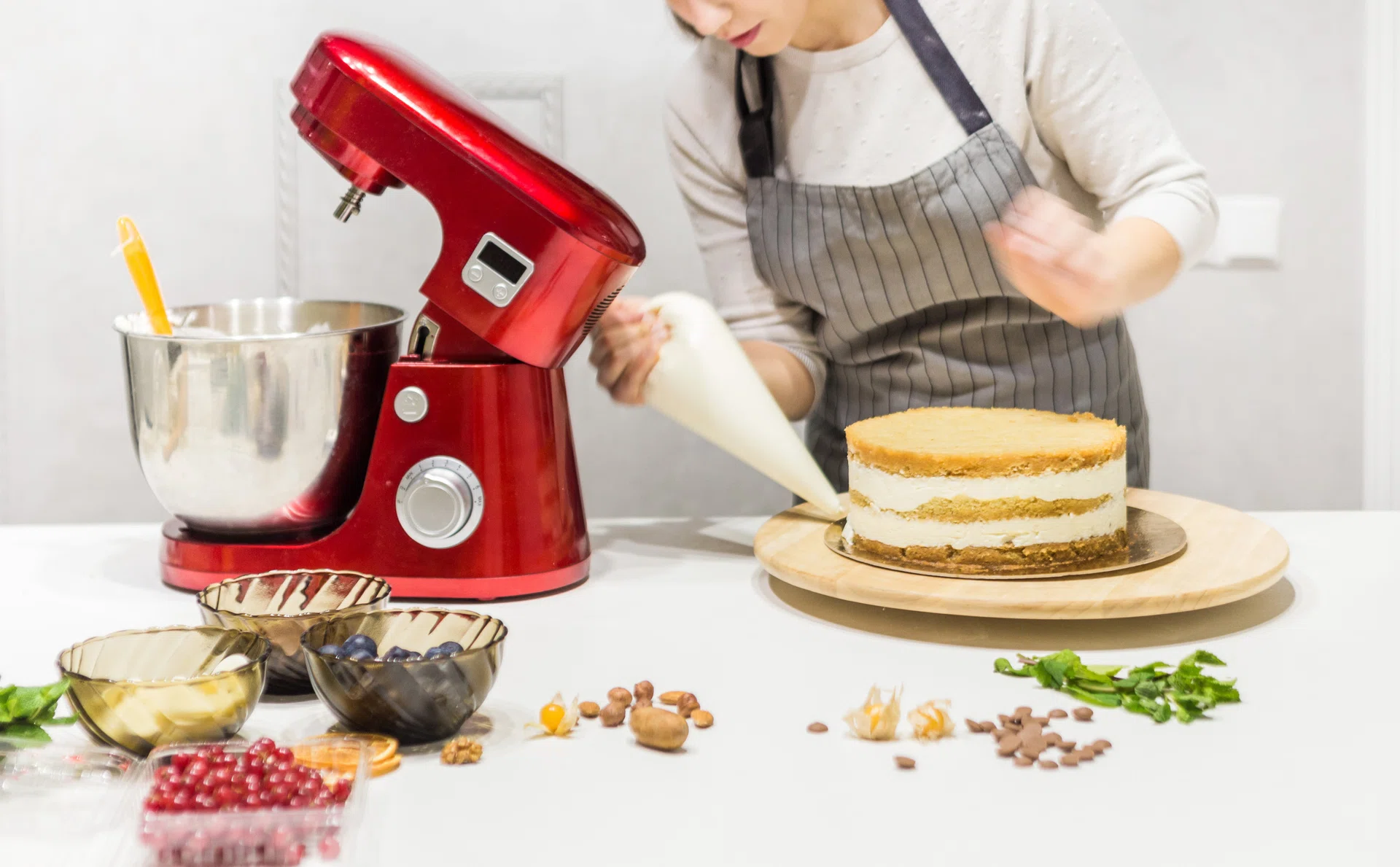 Young female confectioner whips cream in a metal bowl in a red electric mixer. The concept of homemade pastry, cooking.