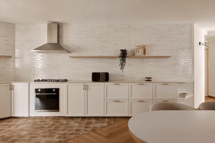 Cream shaker-style cabinetry is paired with glossy gold-flecked wall tiles, while earthy handcrafted-look floor tiles ground the space in understated farmhouse warmth.