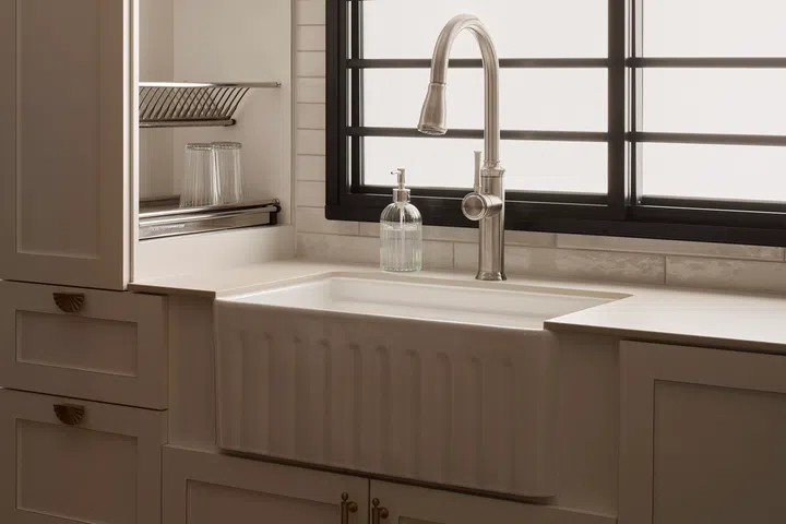 A farmhouse-style apron-front sink sits beneath the window, reinforcing the kitchen’s understated farmhouse character while making the most of natural light.