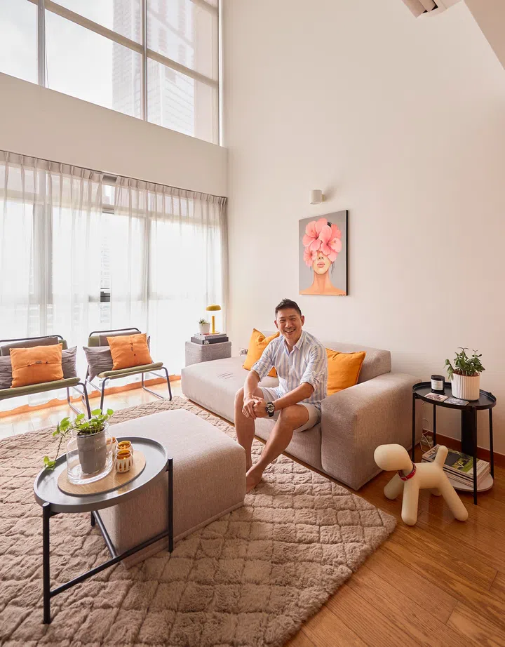 Terence in the double-volume living room, where tall windows flood the loft with daylight and warm orange accents reflect his signature colour palette.