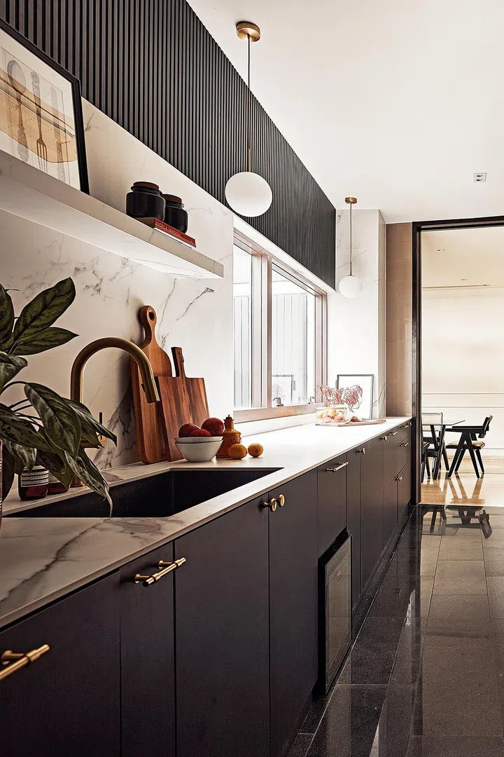 Matte black cabinets with white marble-veined porcelain stone countertops now fill the kitchen. Because the kitchen also has a high ceiling, the design team considered the accessibility of the kitchen cabinets. Instead of installing upper cabinets, the lower kitchen cabinets are complemented with fluted panels on the wall and an easy-to-access shelf.