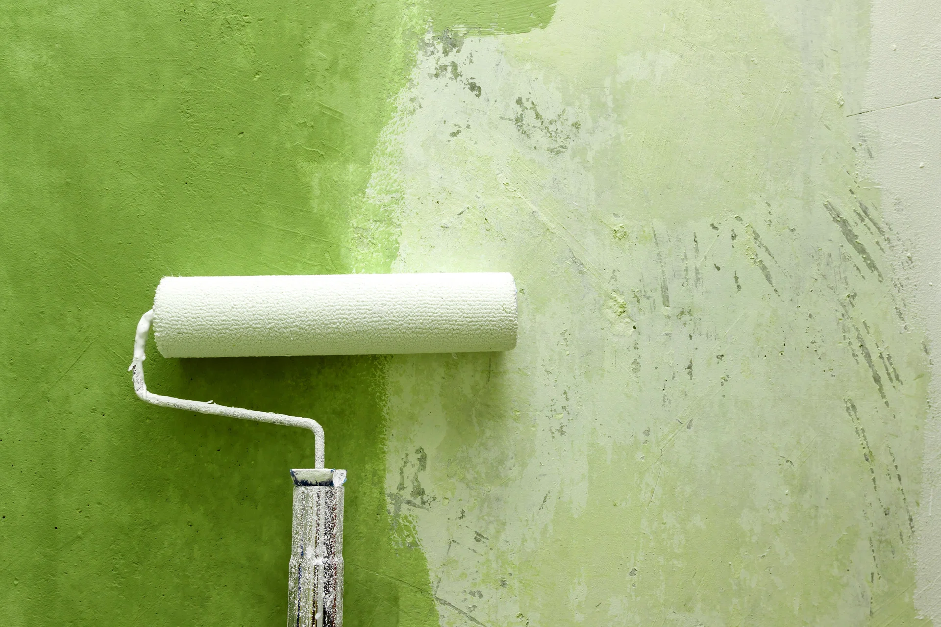 Closeup of paint roller applying green paint on white wall, home improvements, horizontal view.