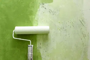 Closeup of paint roller applying green paint on white wall, home improvements, horizontal view.
