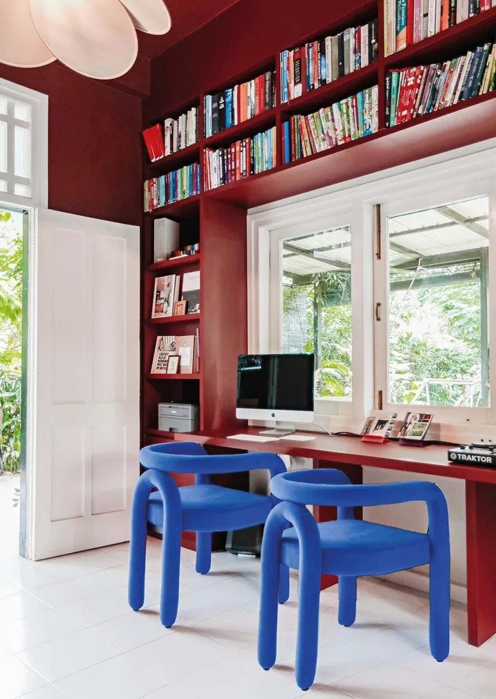 A bookshelf and study table surrounds a window, with 2 blue chairs as a highlight point.
