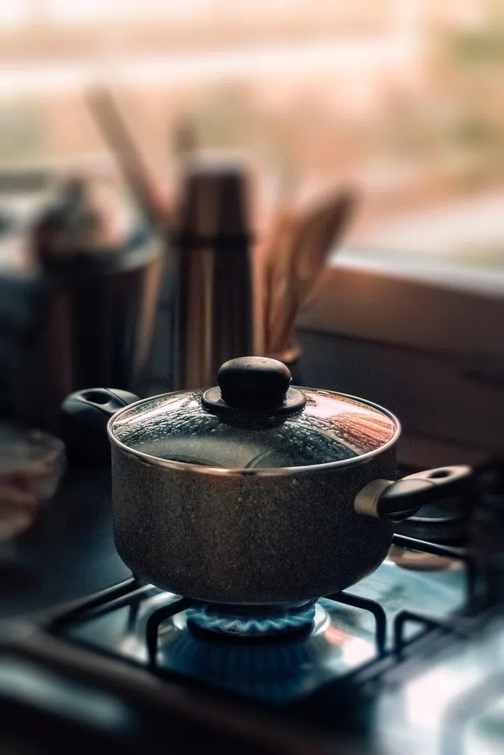 A pot with lid over a gas cooktop stove with fire on.