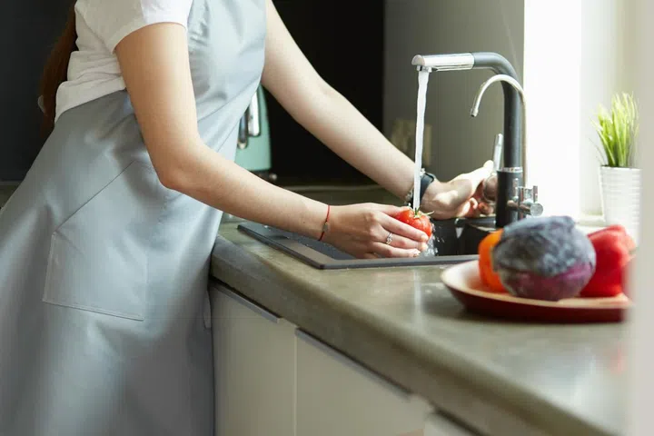 Woman washing tomatoes in kitchen sink close up.