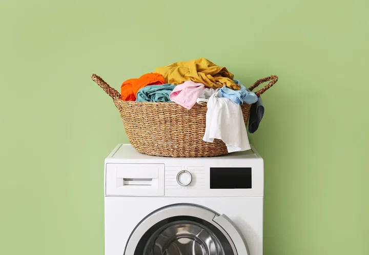 Wicker basket with dirty clothes on washing machine near green wall