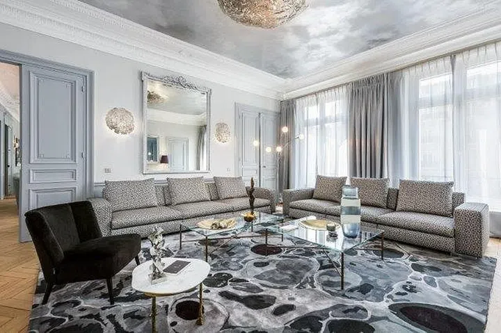 The apartment features a subtle silvery-grey colour palette, and has an ethereal theme inspired by the sky and earth. Ceilings of the living room and lounge are painted in a pattern of a cloudy sky, while contemporary jewellery-like chandeliers and plush rugs with abstract patterns ground the spaces.