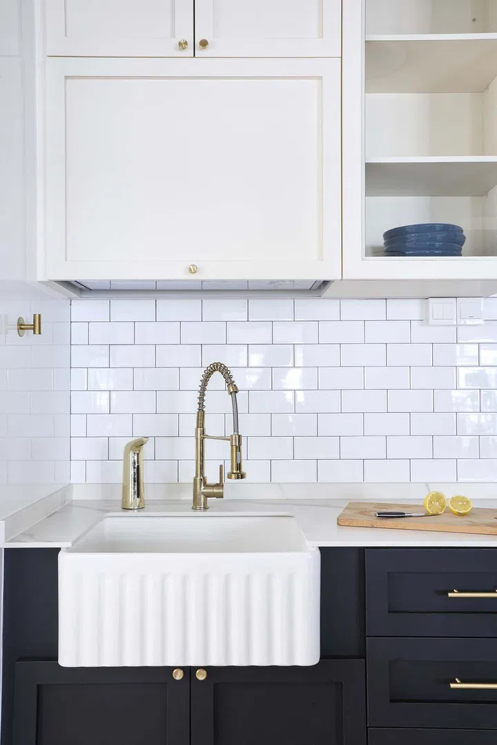 A white farmhouse sink in a black and light cream kitchen for a 32-year-old male homeowner of a 5-room HDB flat in Tampines Avenue 8.