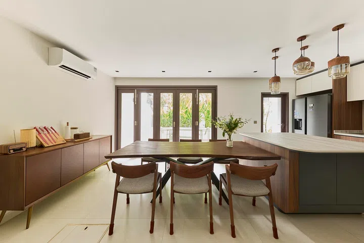 A row of windows draws in natural light and greenery, softening the warmth of timber across the dining and kitchen areas.