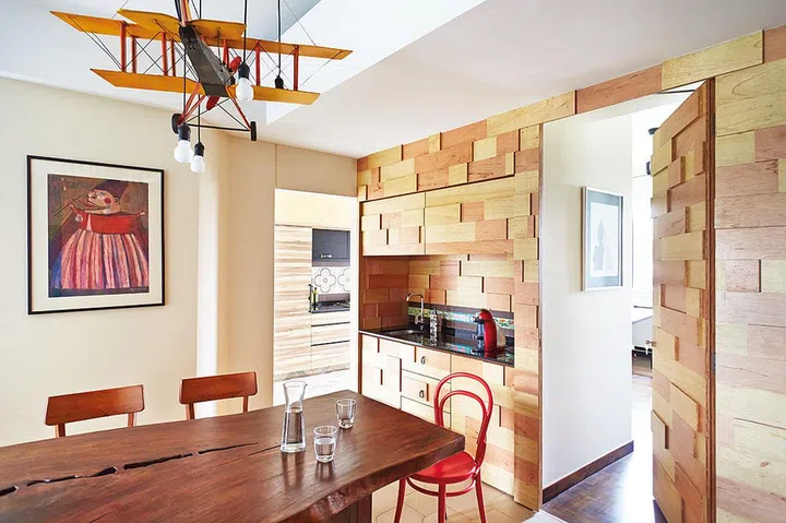 The dining area features a hefty wooden table, under a decorative light fixture composed of a model plane and dangling exposed bulbs.