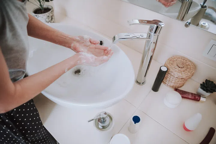 Top view of a water sink in the bathroom used by a woman who is cleaning her hands