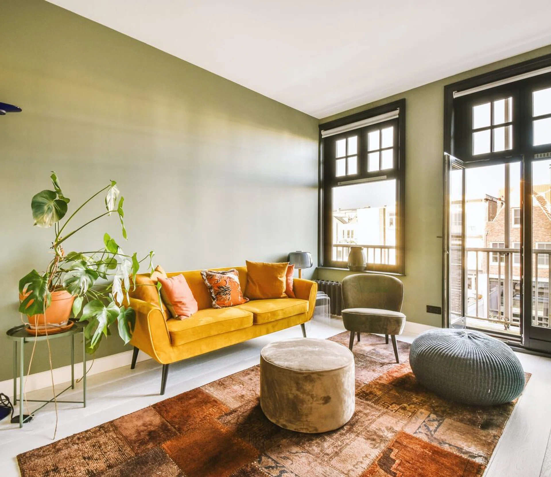 Interior of a bright living room with stylish furniture and decorations, as well as a glass door and black framed windows leading to a balcony on a sunny day