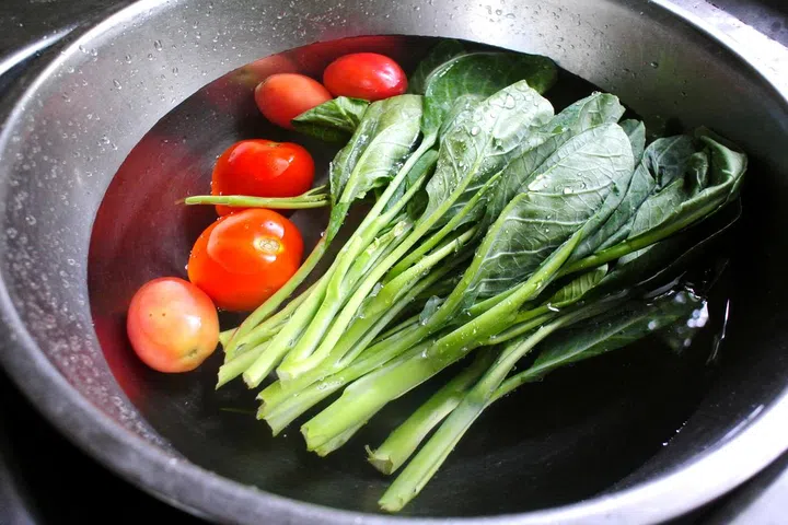 Fresh vegetables lies submerged in a metal bowl.