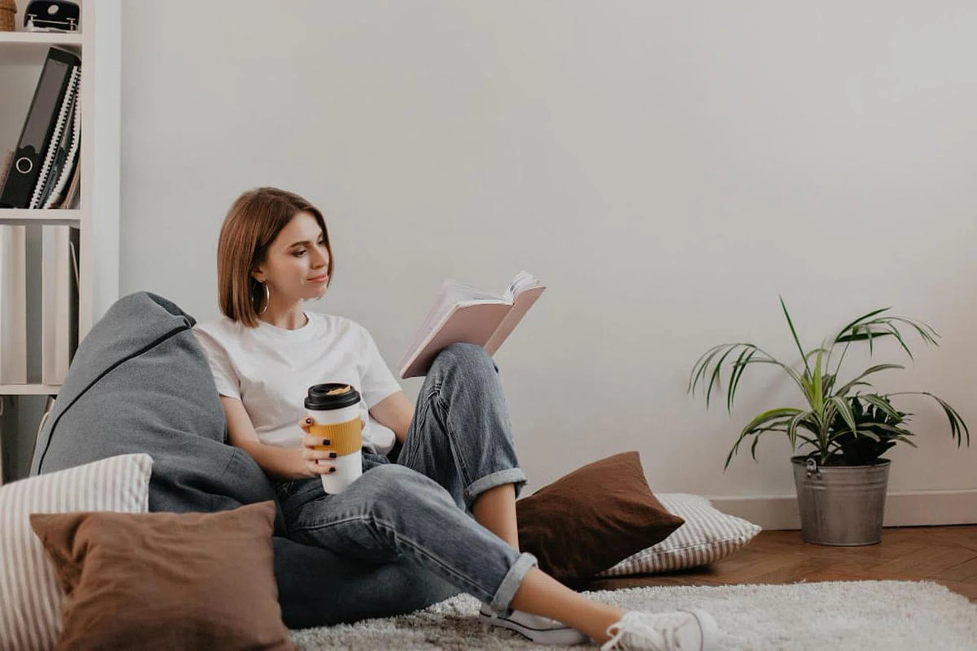 young woman enjoying her coffee and book while sitting on a bean bag. Image from Freepik.