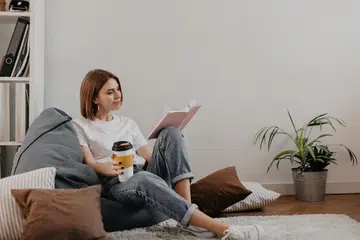young woman enjoying her coffee and book while sitting on a bean bag. Image from Freepik.