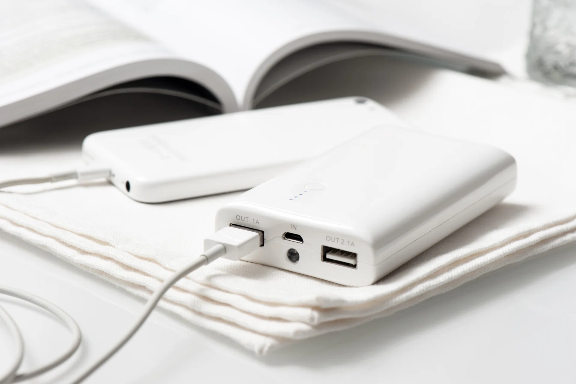A sleek white power bank and smartphone rest elegantly on a soft fabric