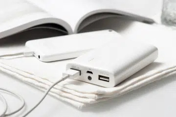 A sleek white power bank and smartphone rest elegantly on a soft fabric