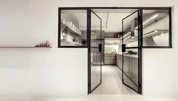 Simple black framed glass doors and windows against stark white walls for a kitchen's entryway. Interior design by 0932 Design Consultants