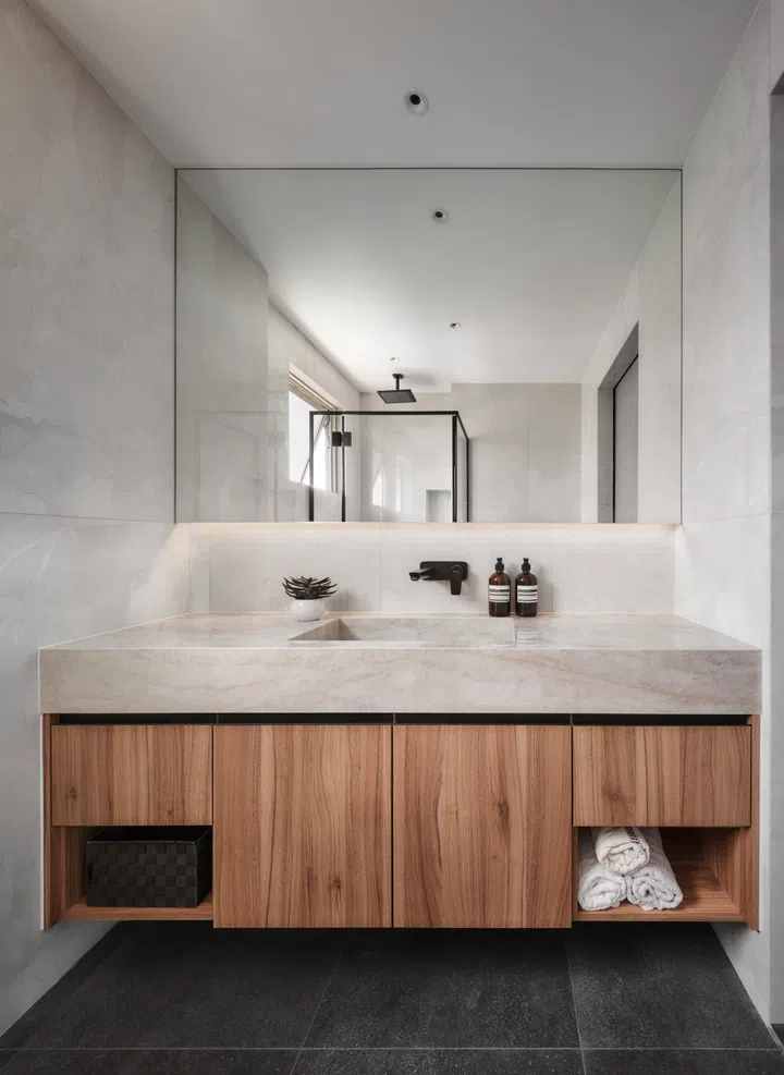 The bathroom pairs a Cosentino stone slab countertop with warm wood cabinetry, balancing luxury with practicality. Slip-resistant flooring and sliding doors make the space future-proof.