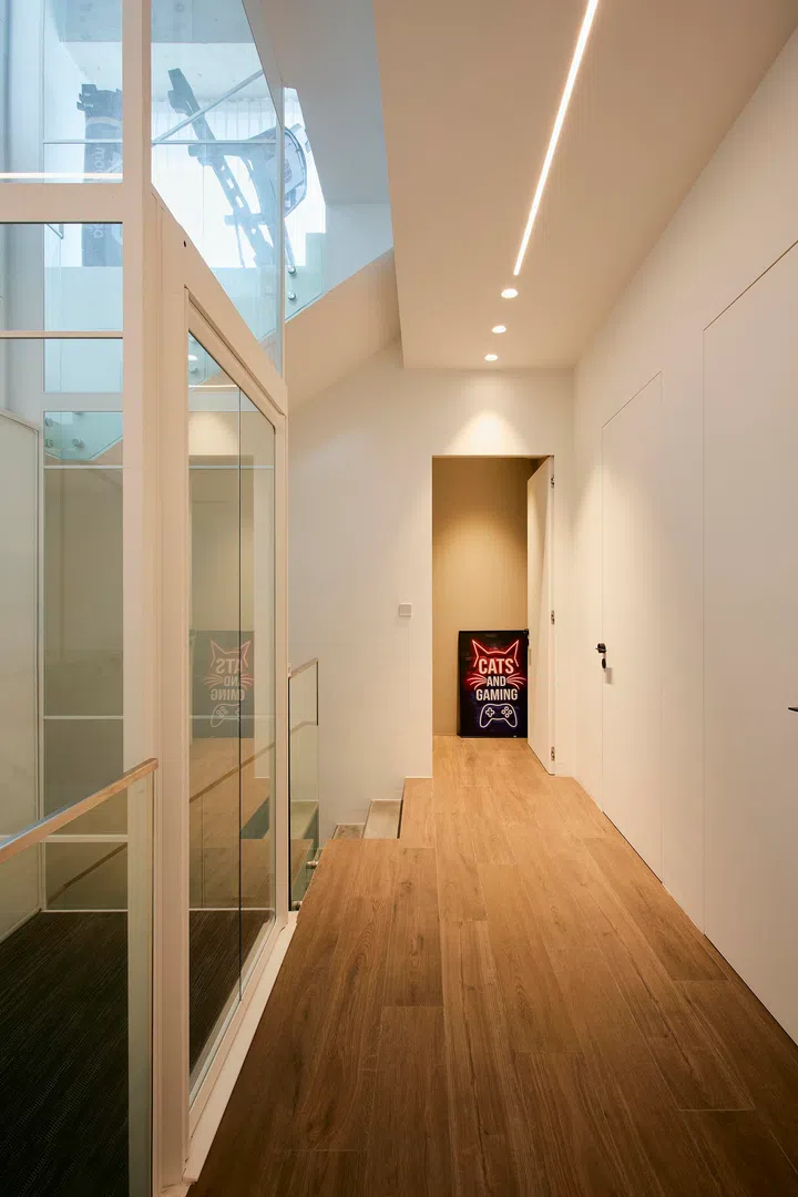 A pared-back corridor beside the glass lift keeps circulation clear and visually connected.