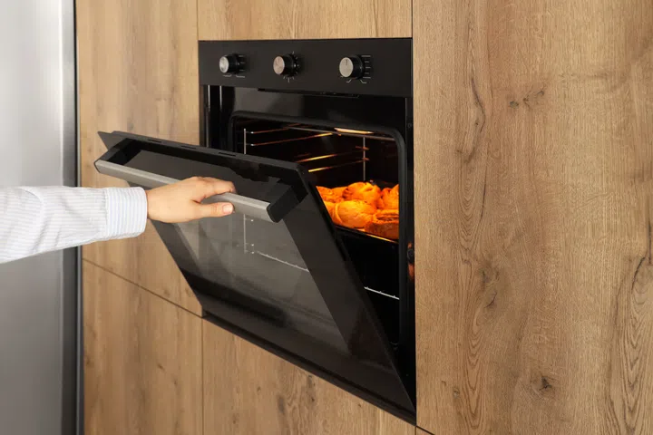 Woman opening oven with buns in kitchen