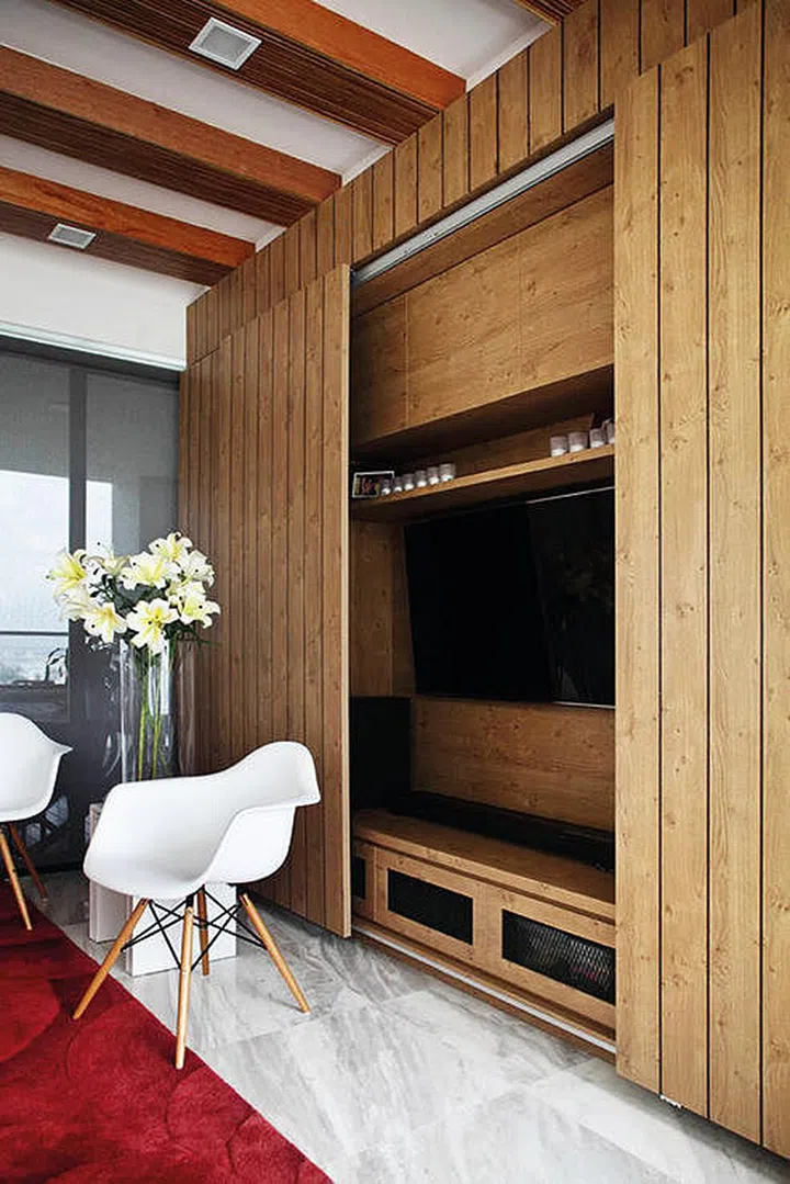 This interior designer created a concealed wooden TV console with sliding doors that gives enough storage space and neatly hides it all away. Interior design by Distinct Identity.