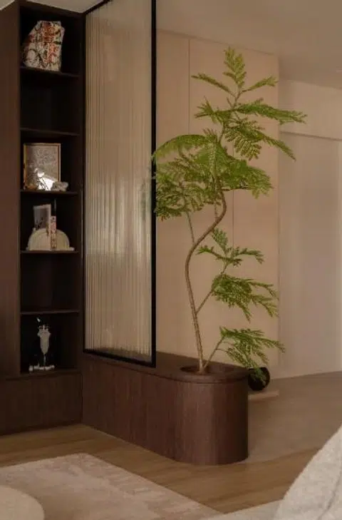 A curved planter and fluted glass screen define the foyer as a soft threshold, allowing light and greenery to filter gently into the living space beyond.