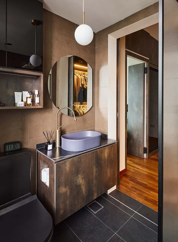 Moody and luxurious master bathroom featuring dark grey tiles, brass fittings, and a ribbed-profile basin, continuing the hotel-inspired look of the bedroom.