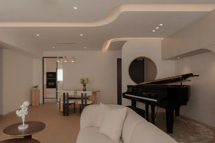 Curved ceiling lines, a sculpted piano alcove, and rounded furniture work together to define living and dining zones while keeping the open-plan layout visually connected.