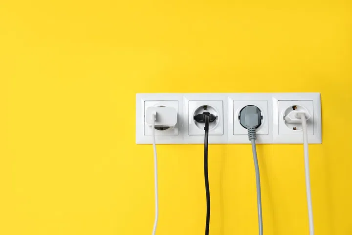 Power sockets with inserted plugs on yellow wall, space for text. Electrical supply