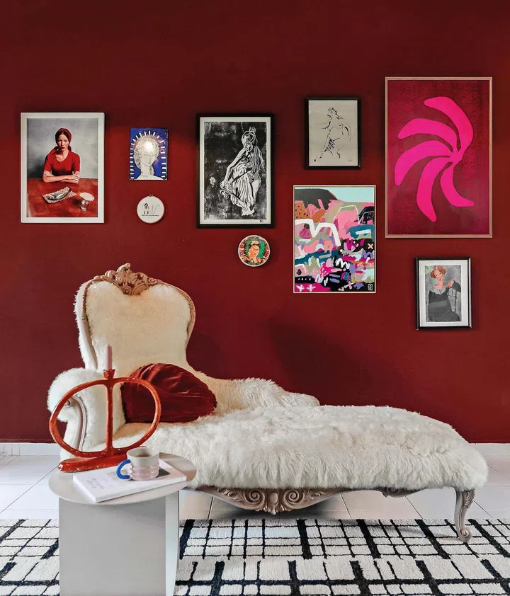 A white fur armchair juxtaposed with a deep red wall with various paintings.