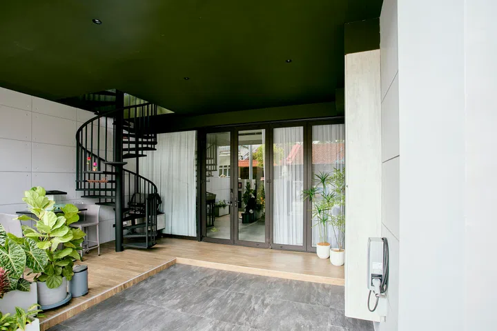 A spiral staircase anchors the semi-outdoor entry zone, where sliding glass doors and full-height curtains mark the shift from exterior to interior.