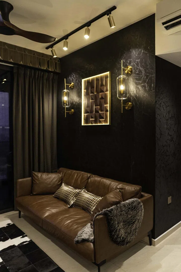 A plush leather sofa, cowhide rug, brass-finished lighting set against a black wallpaper in a banking couple's 3-bedroom condominium in West Coast.