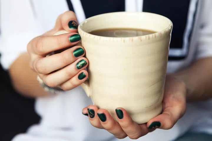 Stylish fashionable girl with a Cup of coffee and a green manicure in jeans. Fashion, care, beauty