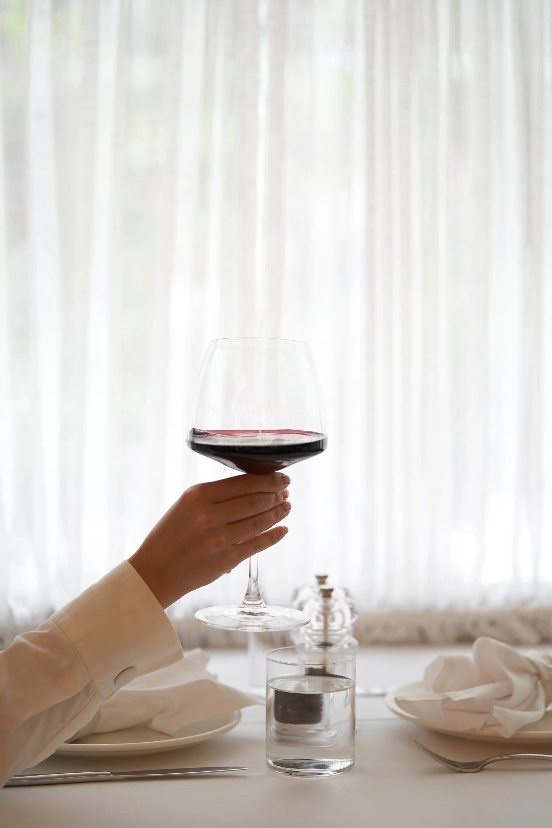 Woman holding glass of red wine at table indoors.