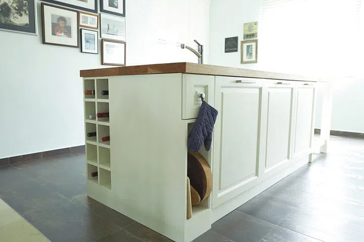 The stove, sink and refrigerator sit in a linear layout, while an island countertop provides additional storage for pots, pans and wine bottles. This island also doubles as a food preparation and breakfast counter. The cabinets are solid wood spray-painted white.