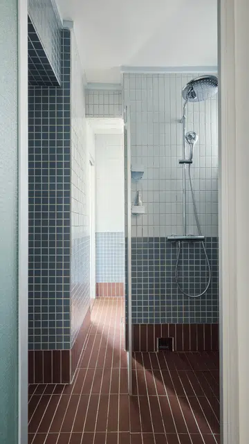 A narrow passageway connects the toilet and vanity to the shower area, allowing the bathroom to be accessed from both the kitchen and bedroom.