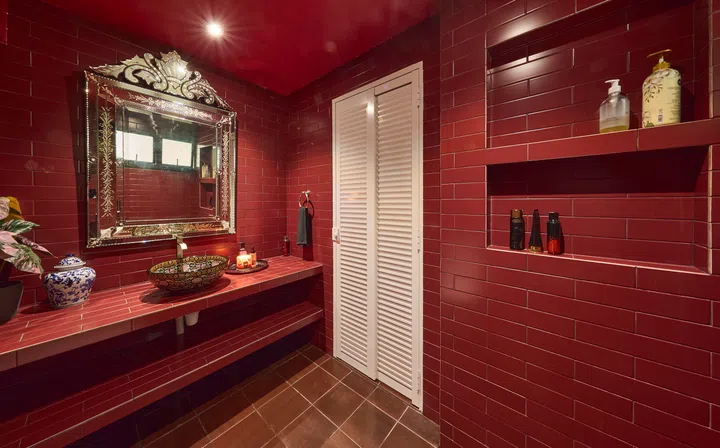 The master bathroom is fully drenched in deep red, with tiles extending across walls and ceiling to create a cocoon-like space.