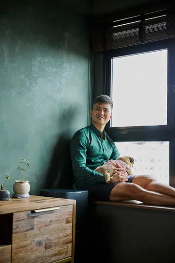 Bruce, aviation firefighter in his early 30s, and his pug poses for a photo by the window.